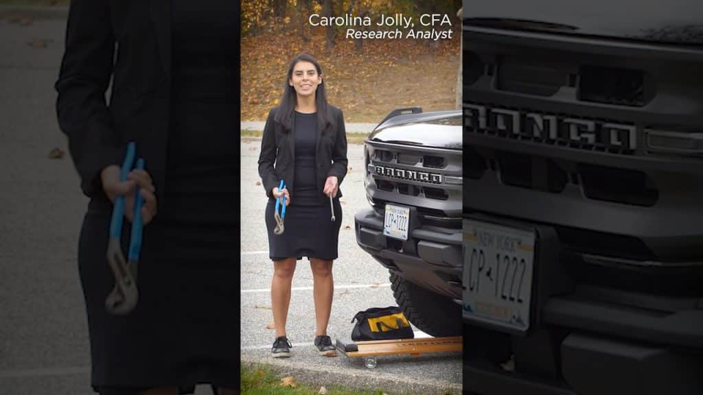 a woman with tools working on her car wearing a dress and a blazer