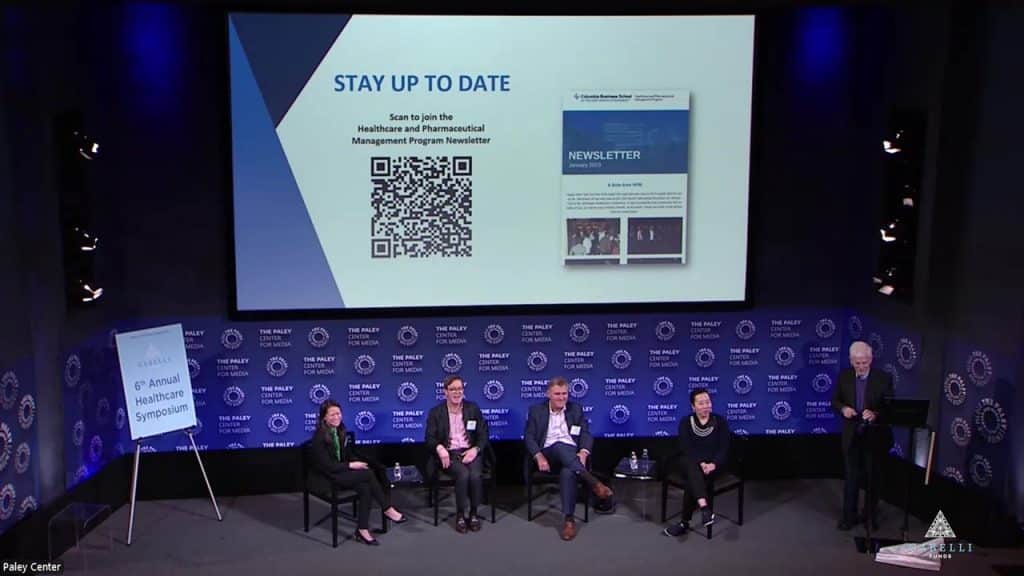 speakers on stage with a slide deck presentation at a symposium