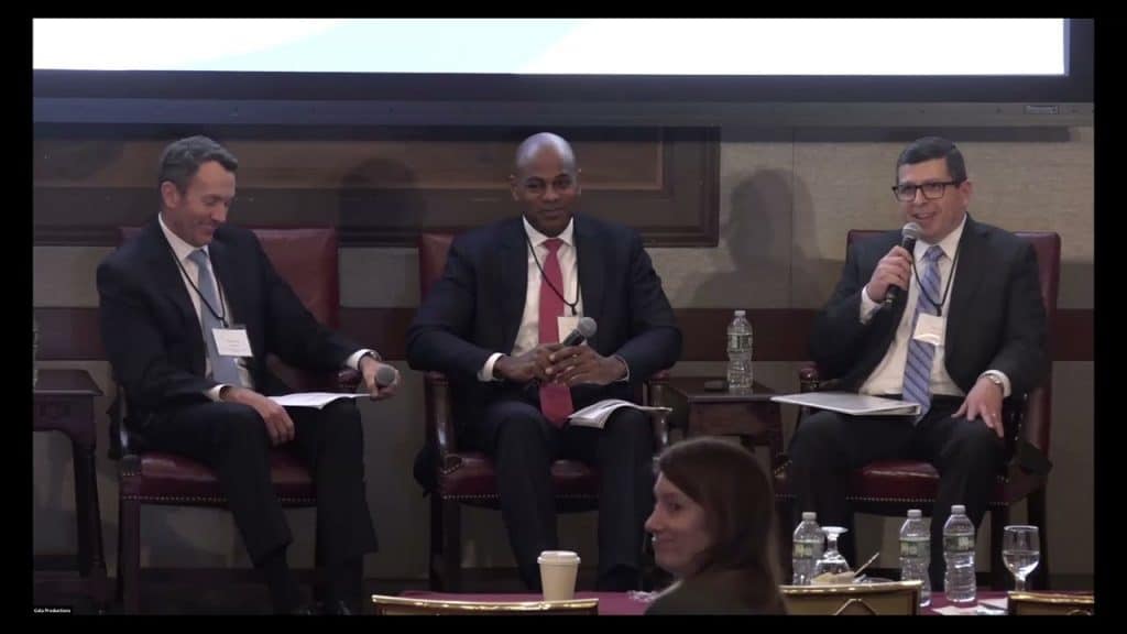 photo of three men on a stage speaking at a symposium