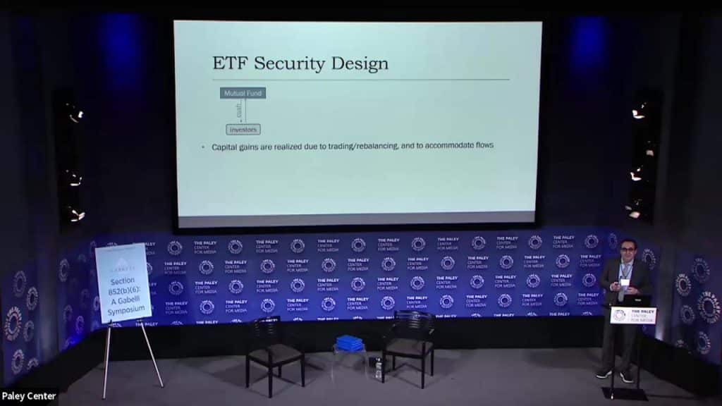 a person speaking on stage with a slide deck presentation at a symposium